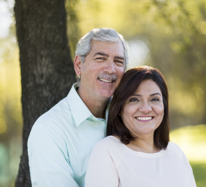 Man and woman hugging and smiling with tree in background