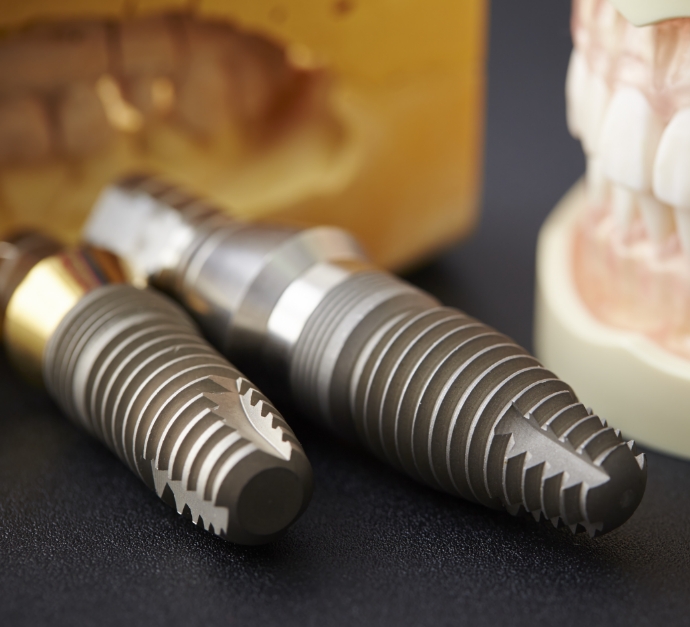 Two dental implants resting on table next to model of dentures