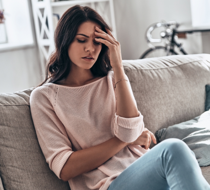 Wincing woman sitting on couch and holding her head in pain