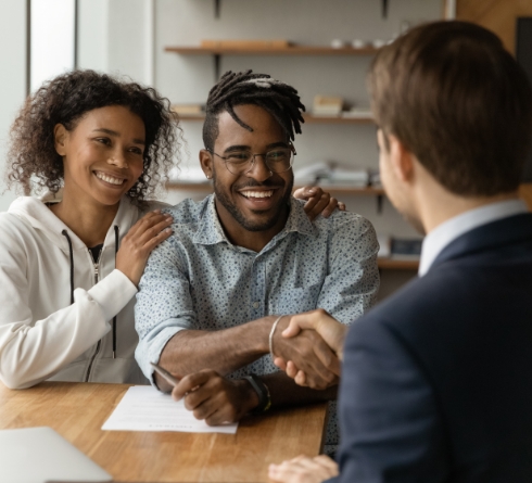 Smiling man shaking hands with person sitting across desk