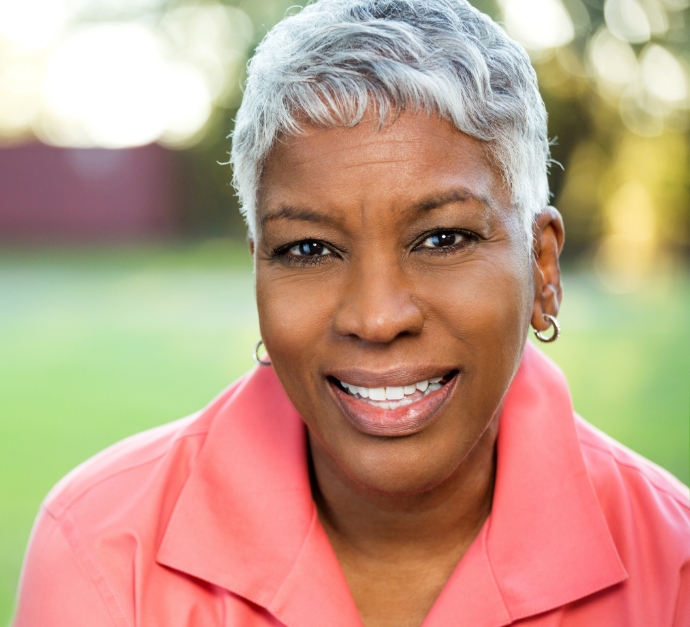 Older woman in orange collared shirt smiling outdoors