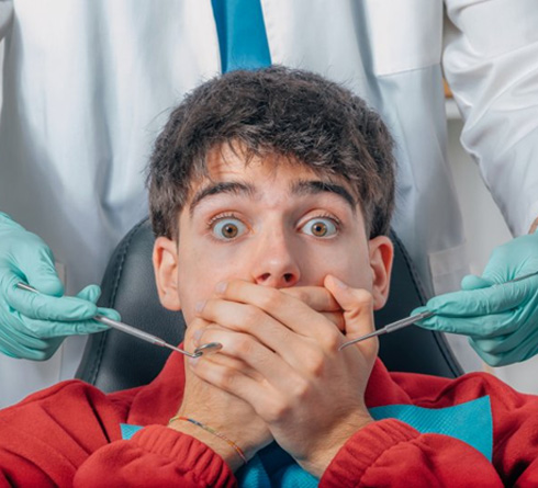 Anxious patient covering their mouth while dentist holds dental tools