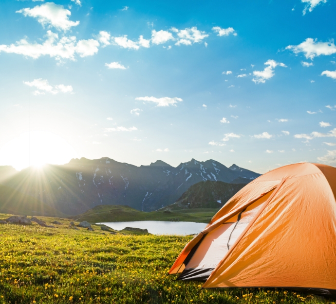 Orange camping tent on a hill with mountains in the background