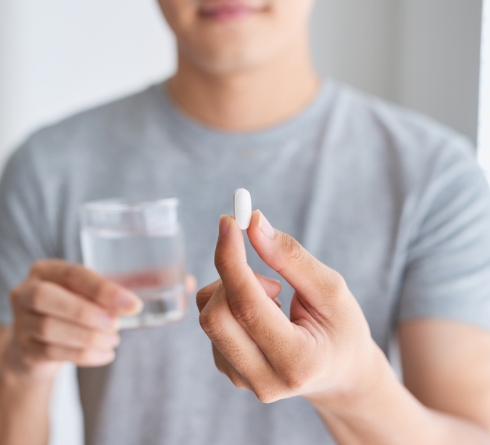 Man holding glass of water and white pill