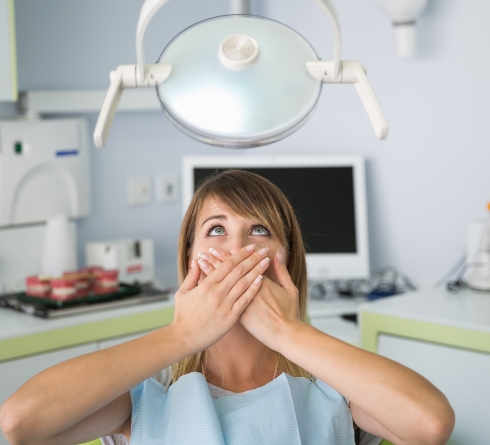 Nervous woman in dental chair covering her mouth
