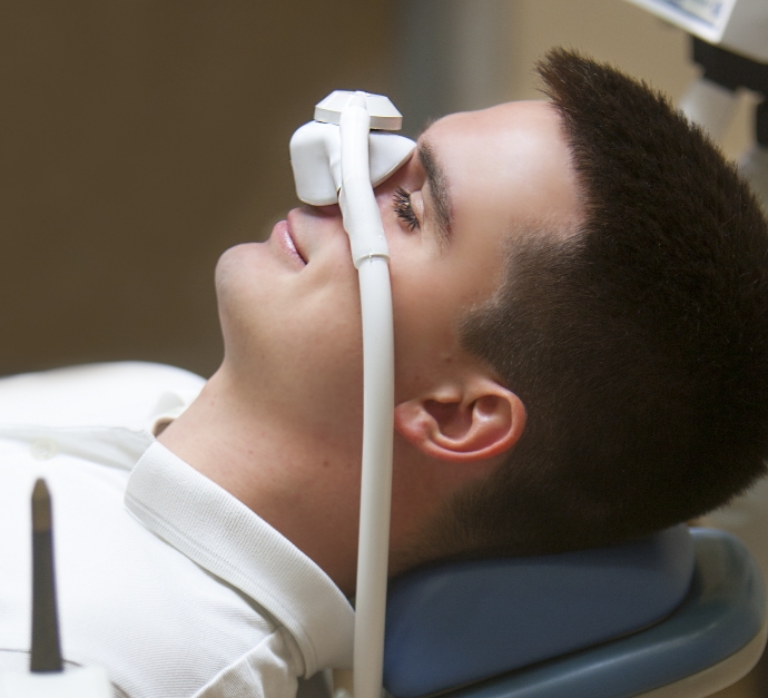 Man in dental chair with eyes closed and nitrous oxide mask on his nose