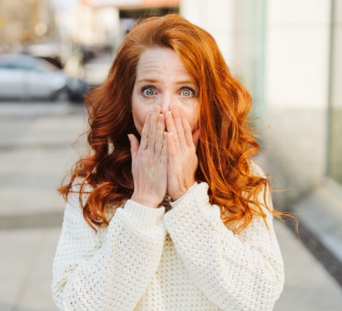 Redheaded woman on city sidewalk covering her mouth
