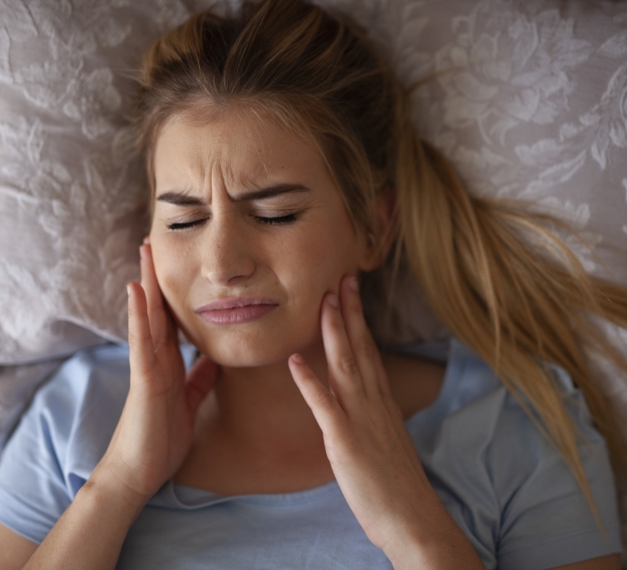 Woman winning and holding her face in pain before tooth extractions in Staten Island