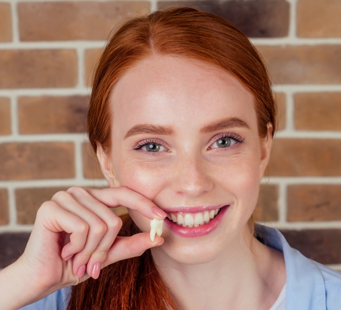 Smiling woman holding her extracted tooth