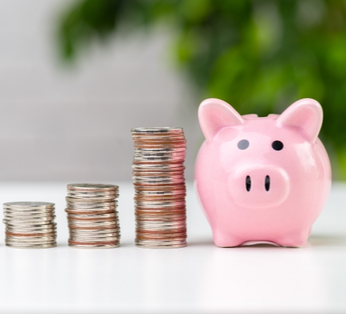 Pink piggy bank next to three stacks of coins