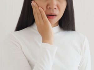 Woman with brown hair and white shirt holding the palm of her hand to her jaw