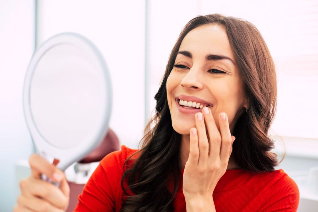 A woman smiling in a mirror at her dental implants